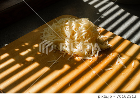 Grated cheese on wooden board. Stripes from blinds 70162512