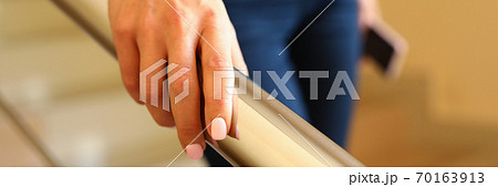 Businesswoman comes down stairs and holds on to handrail 70163913