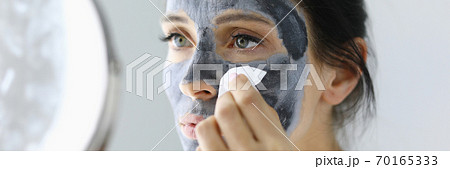 Woman looks in mirror and rinses off cosmetic mask. 70165333