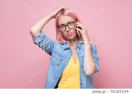 woman in glasses talking on the phone being puzzled. 70165334