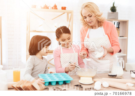 Grandchildren and grandmother prepare a dish. Grandchildren and grandmother prepare a dish. 70166978