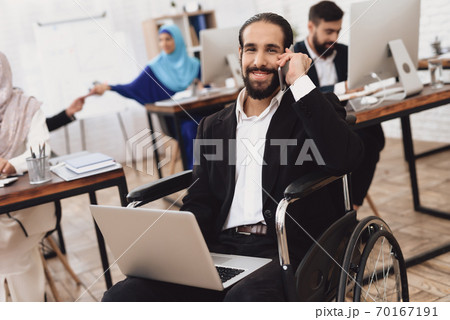 A man sits in a wheelchair with a laptop. 70167191