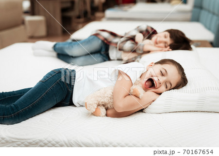 Girl yawns while sleeping on a bed in a store. 70167654