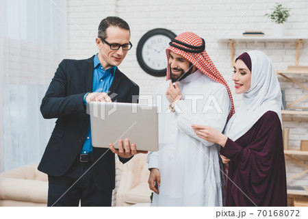 A man shows Arab couple something on a notebook. A man shows Arab couple something on a notebook. 70168072