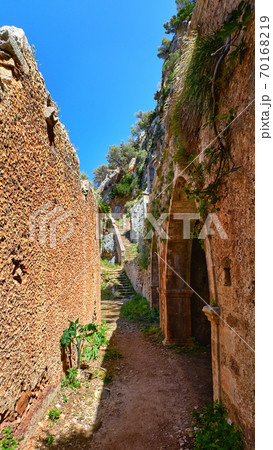 Walkway in ruins of remote abandoned Katholiko monastery in Avlaki gorge of Akrotiri peninsula, Chania, Crete, Greece. Wild spring foliage, clay walls 70168219