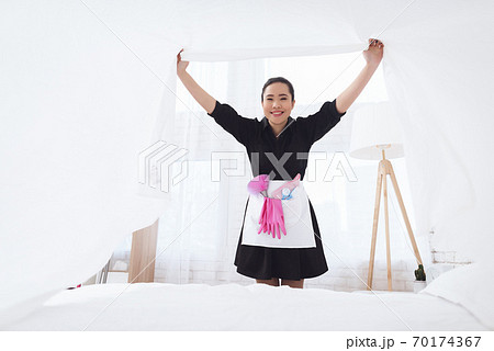 Asian housekeeper makes a bed and rejoices. Asian housekeeper makes a bed and rejoices. 70174367