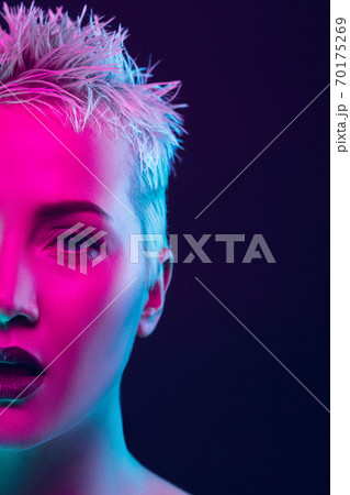 Portrait of female fashion model in neon light on dark studio background. 70175269