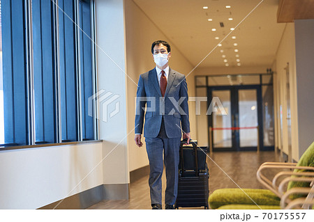 マスクをして出張でキャリーカートを引いて歩くビジネスマン マスクをして出張でキャリーカートを引いて歩くビジネスマン 70175557