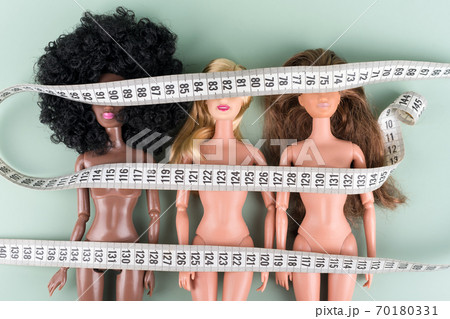 Dolls wrapped in measuring tape. Unrecognizable fashion dolls, weight loss concept. Fasting, weightloss and slimming. Diet, anorexia, eating disorder, overeating control, fight for perfect fit body. Dolls wrapped in measuring tape. Unrecognizable fashion dolls, weight loss concept. Fasting, weightloss and slimming. Diet, anorexia, eating disorder, overeating control, fight for perfect fit body. 70180331
