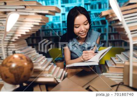 A student sits surrounded by books and writes. 70180740