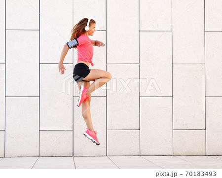 Dynamic sporty woman with headphones jumping near wall. Dynamic sporty woman with headphones jumping near wall. 70183493