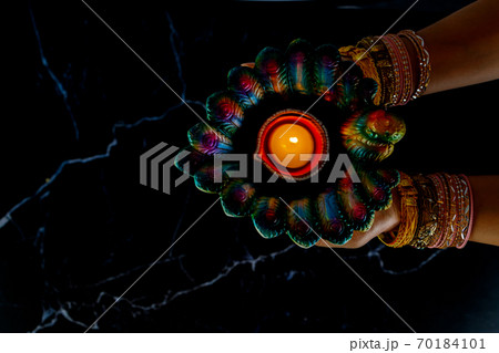 Happy Diwali - Woman hands with henna holding lit candle isolated on dark background. 70184101