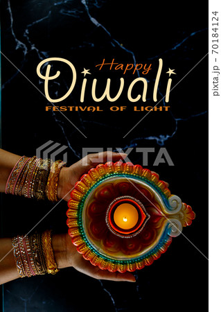 Happy Diwali - Woman hands with henna holding lit candle isolated on dark background. 70184124
