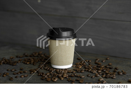 Paper cup of coffee with roasted coffee beans on wooden table background. Mug of black coffee. 70186783