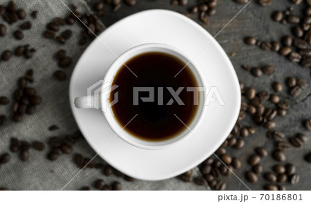 Coffee cup with roasted coffee beans on wooden table background. Mug of black coffe with scattered coffee beans on a wooden table. Fresh coffee beans. 70186801