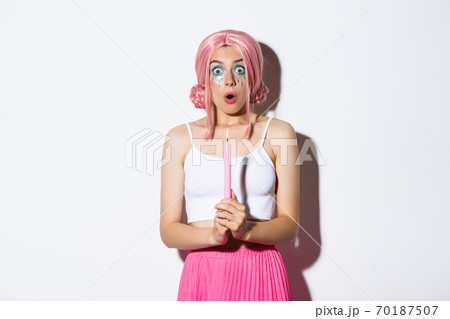 Portrait of shocked girl casting magic spells on halloween, holding candle and looking amazed, standing in costume with pink wig and bright makeup 70187507