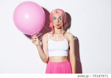 Image of silly party girl with bright makeup, pink wig, holding big cute balloon and pouting, standing over white background Image of silly party girl with bright makeup, pink wig, holding big cute balloon and pouting, standing over white background 70187671