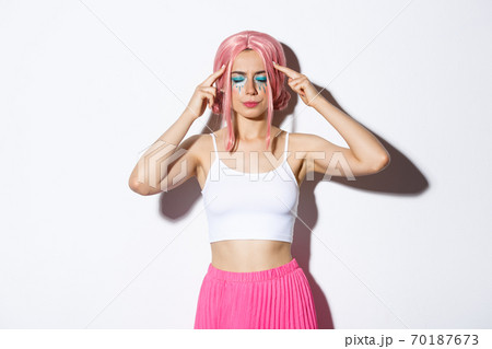 Portrait of distressed caucasian girl with pink wig and party makeup, standing with closed eyes and touching head, trying to think or remember something Portrait of distressed caucasian girl with pink wig and party makeup, standing with closed eyes and touching head, trying to think or remember something 70187673