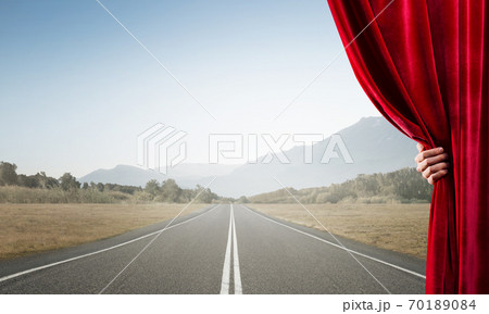 Asphalt road behind red curtain and hand holding it 70189084