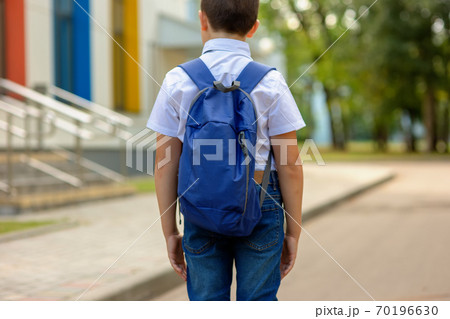 A brunette schoolboy in a white shirt and blue backpack goes to school 70196630