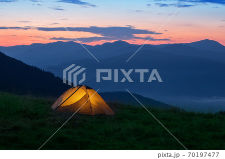 Orange tourist tent illuminated from inside on mountain 70197477