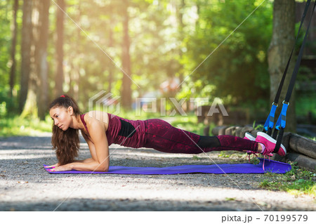Young woman performs a plank exercise with fitness straps in the fresh air. Healthy lifestyle concept Young woman performs a plank exercise with fitness straps in the fresh air. Healthy lifestyle concept 70199579