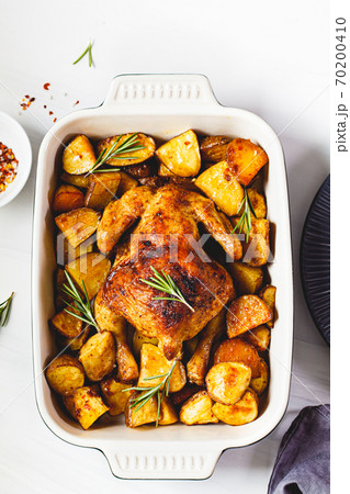 Baked whole chicken with potatoes and rosemary in black dish, white background, top view. 70200410