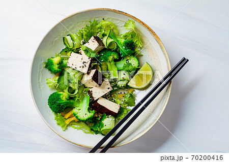 Green Asian salad with broccoli and smoked tofu in white bowl, white background. 70200416