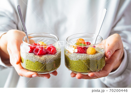 Woman holding matcha tea chia seeds pudding with raspberries in glass jars. Healthy food concept. Woman holding matcha tea chia seeds pudding with raspberries in glass jars. Healthy food concept. 70200446