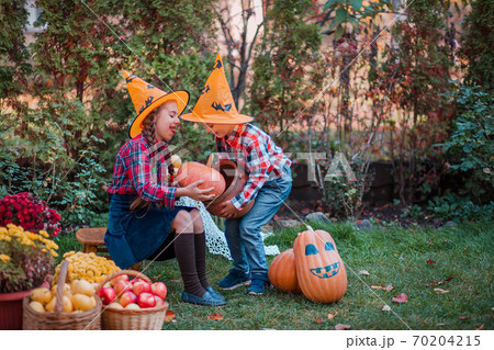 Brother and sister play in the Autumn Garden, surrounded by fruits of vegetables and fruits. 70204215