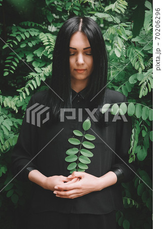 Beautiful girl in black dress that holds a twig in her hand against the background of the forest 70206296
