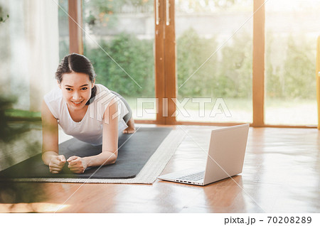 woman doing plank exercise at home while watching online workout session from laptop 70208289