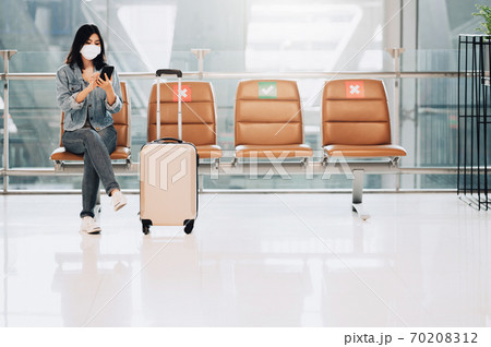 Woman traveler wearing mask sitting on social distancing chair using smartphone 70208312