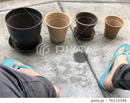 ベランダに大きさ順で並べられた植木鉢とサンダル履きの足の写真素材