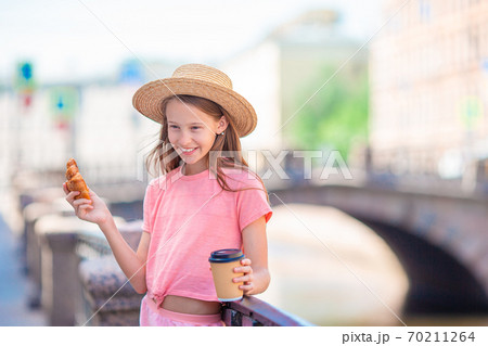 Woman with a croissant and coffee outdoors on the promenade Woman with a croissant and coffee outdoors on the promenade 70211264