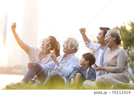 three generation happy asian family sitting on grass taking selfie using cellphone outdoors in park three generation happy asian family sitting on grass taking selfie using cellphone outdoors in park 70212029