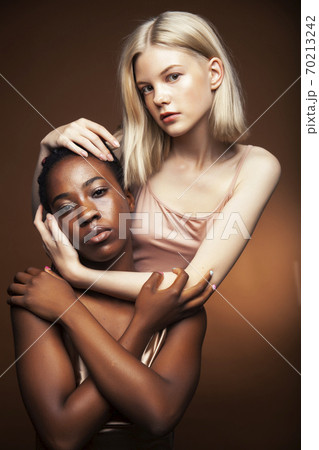 two pretty girls african and caucasian blond posing cheerful together on brown background, diverse lifestyle people concept two pretty girls african and caucasian blond posing cheerful together on brown background, diverse lifestyle people concept 70213242