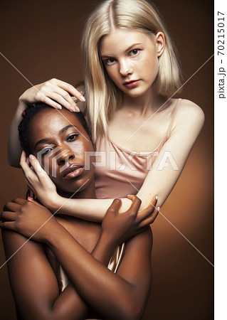 two pretty girls african and caucasian blond posing cheerful together on brown background, etnithity diverse lifestyle people concept two pretty girls african and caucasian blond posing cheerful together on brown background, etnithity diverse lifestyle people concept 70215017