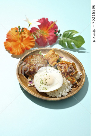 チキンナゲットやナポリタンも一緒に乗っている熱々のロコモコ丼とハイビスカスの造花 70216596