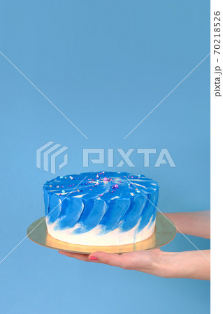 Girl's hands are holding beautiful and tasty cake with white and true blue color cream on a blue background with place for text. 70218526