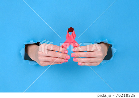 Red ribbon is symbol of fight against AIDS or disease cancer of female breast. Girl's hand holds a red ribbon on a blue torn papper background. Copy space aside for your advertising content 70218528