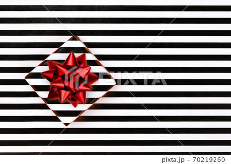Top view of gift box on striped paper with red bow. 70219260