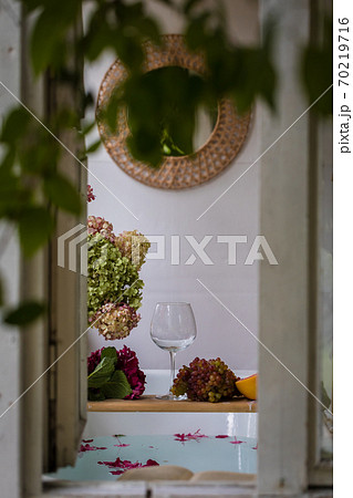 Bath tub with flower petals, grapefruit slices, bunch of grapes and a glass Bath tub with flower petals, grapefruit slices, bunch of grapes and a glass 70219716