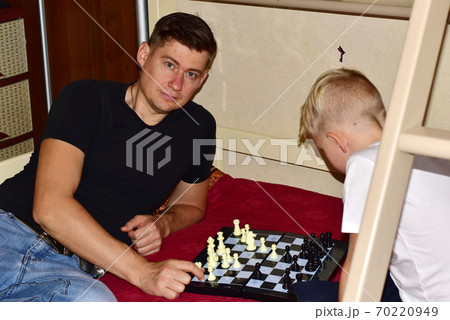 Boy and dad are playing chess on the bed in the room. Boy and dad are playing chess on the bed in the room. 70220949