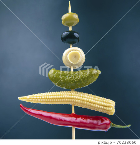 Olives, pickled cucumber, red hot peppers, mushrooms and corn on a wooden stick close-up on a dark background. food and vegetables Olives, pickled cucumber, red hot peppers, mushrooms and corn on a wooden stick close-up on a dark background. food and vegetables 70223060