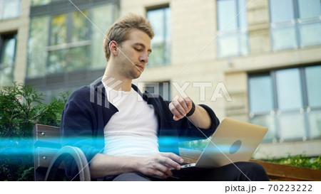 Young man with laptop consulting his watch, background of house lens flare 70223222