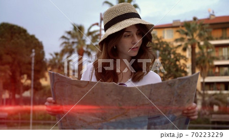 Young woman in hat holding looking at a map, south city in France, lens flare 70223229