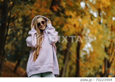 Beautiful happy smiling young woman wearing pink hoodie walking in autumn park. Season and people concept. Beautiful happy smiling young woman wearing pink hoodie walking in autumn park. Season and people concept. 70223404