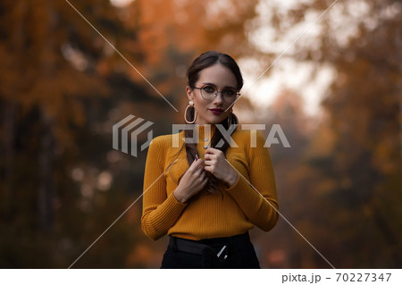 Charming young woman standing in autumnal park Charming young woman standing in autumnal park 70227347