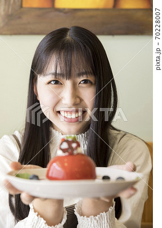 カフェで可愛いケーキを見せる若い女性 女子大生の写真素材